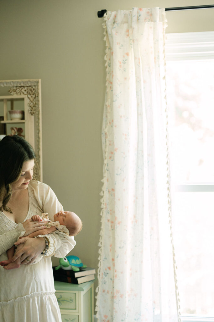 Mother holding her newborn beside a bright window at home