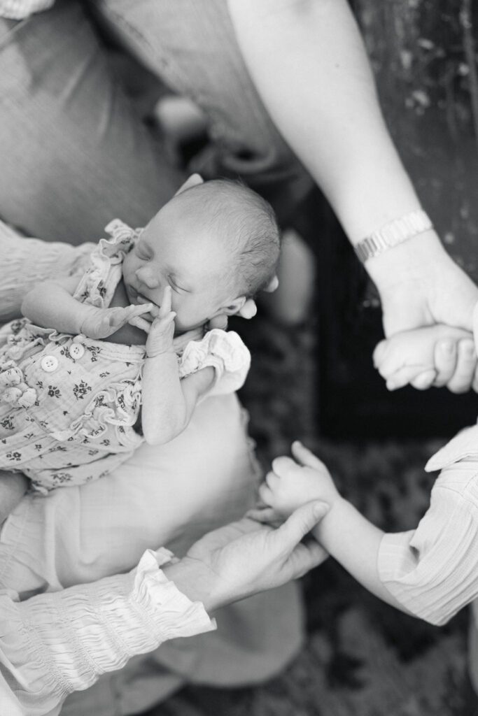 Newborn baby resting between a parent's hands in a black and white portrait